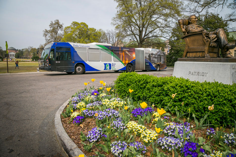 A campus shuttle bus makes a stop on campus, circling around a flower garden.