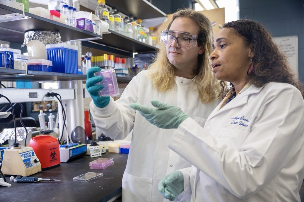 Two people in lab coats standing next to the bench, holding up and inspecting their work.