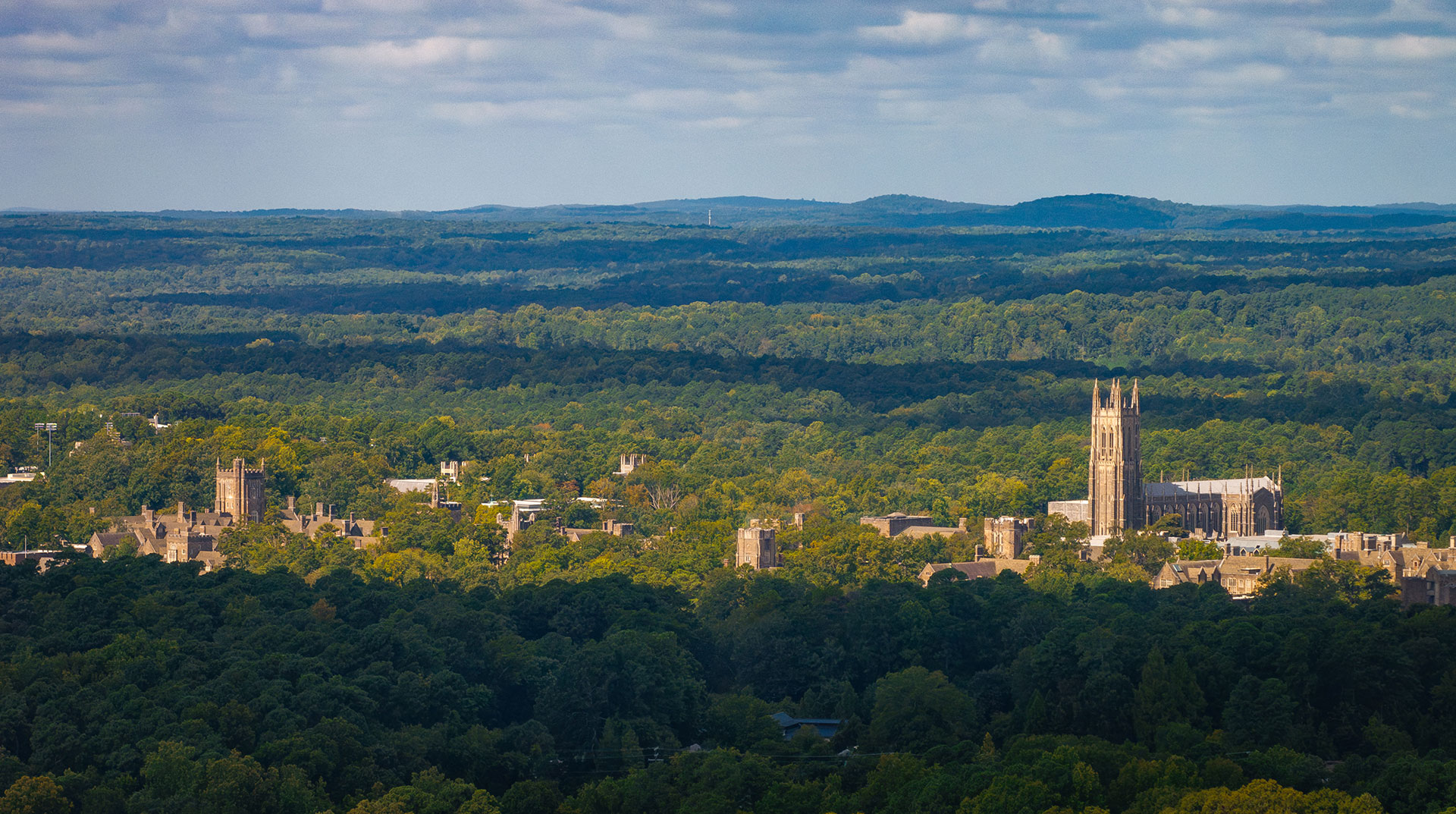 An aerial view of West Campus surrounded by green trees with mountains in the distance
