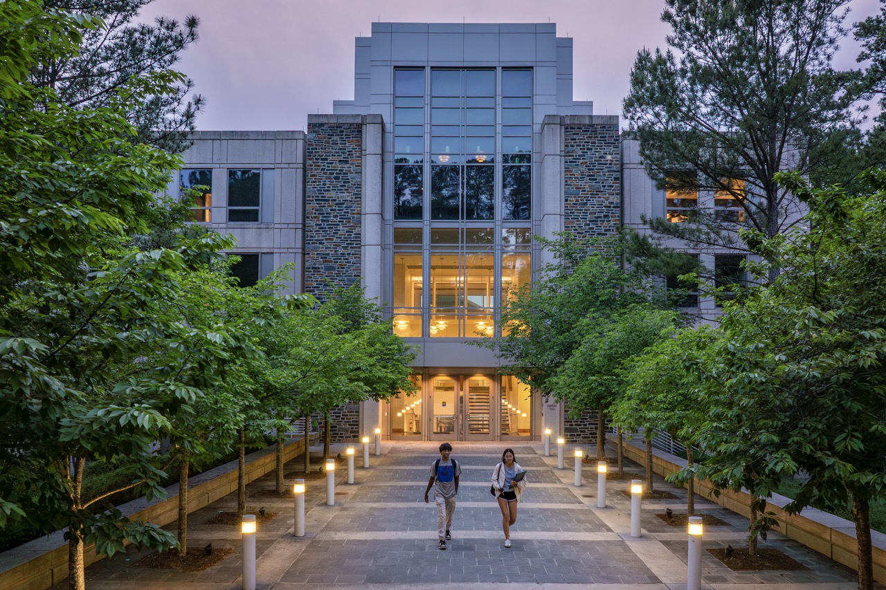Two students walking out of the Fuqua School of business at dusk