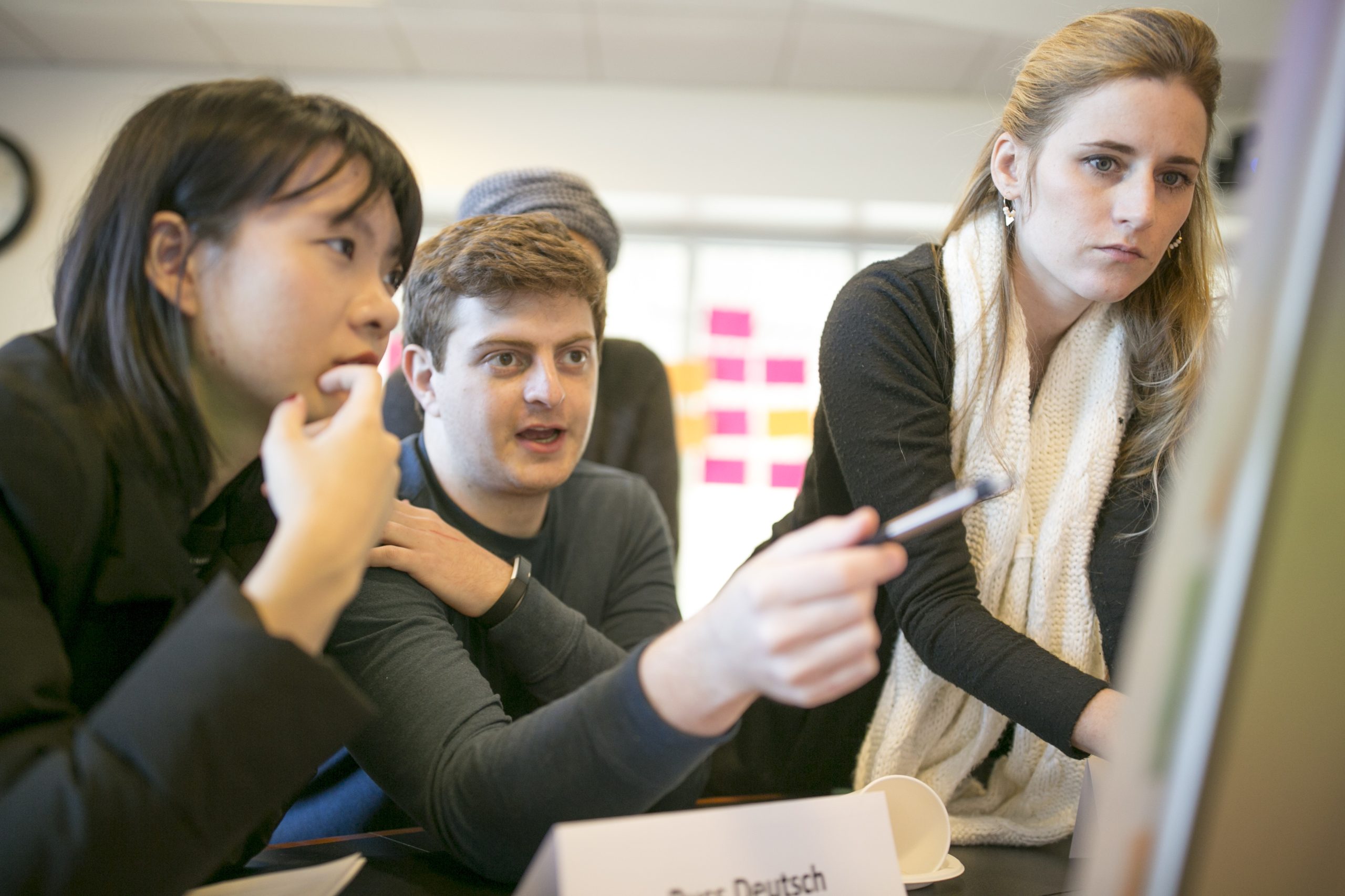 Three students participating in a law class—the one in the middle pointing at an easel with a pen