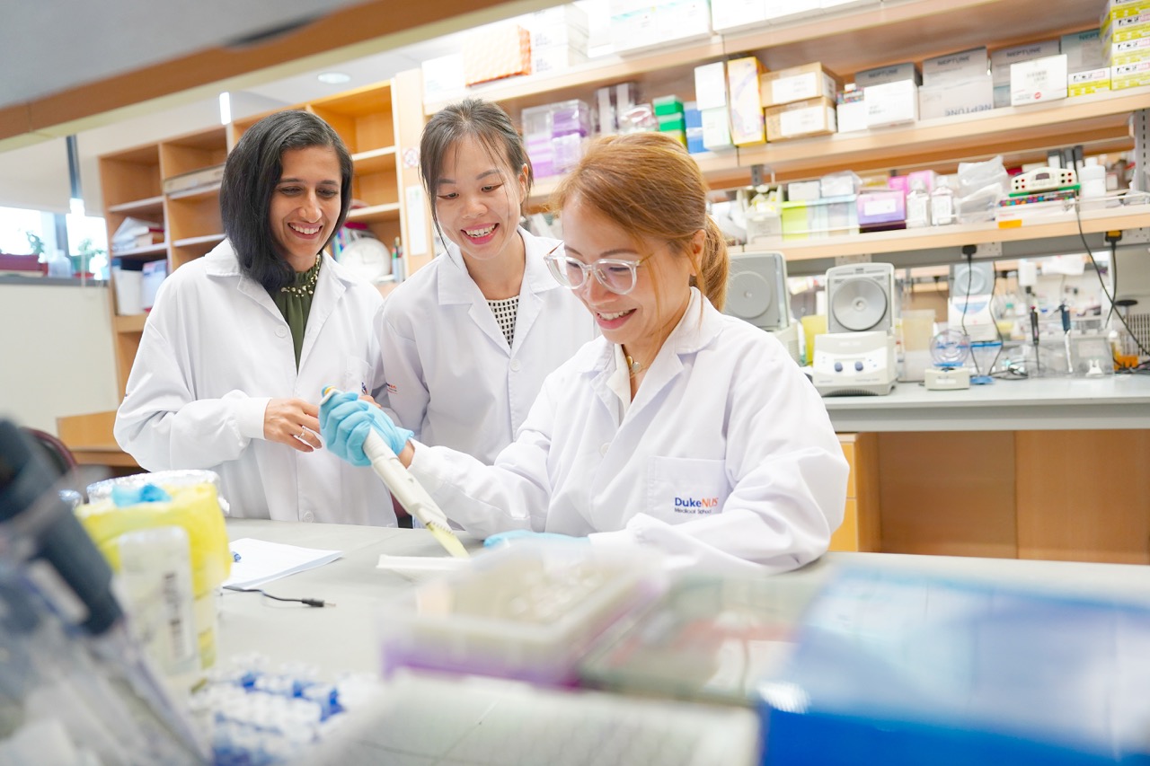 Three students in lab coats working at a lab bench