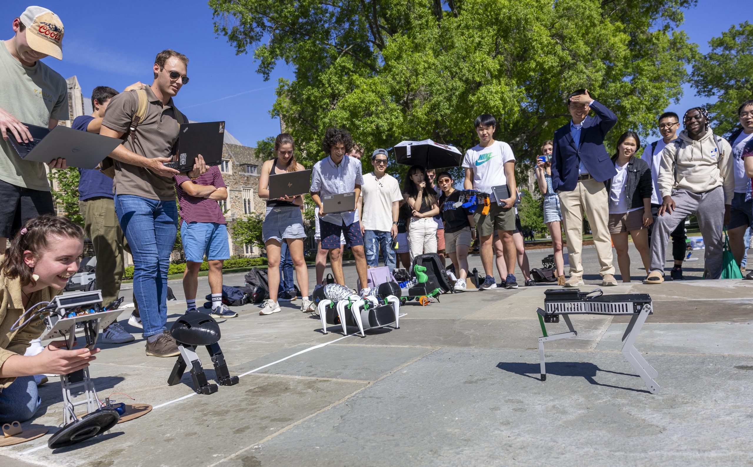 Engineering students stand around a group of robots on the quad