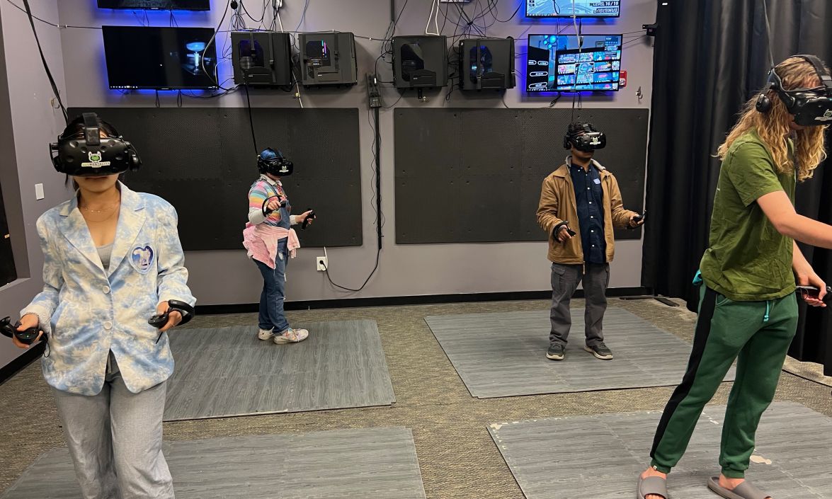 4 people standing in a room with screens and wires using virtual reality headsets.