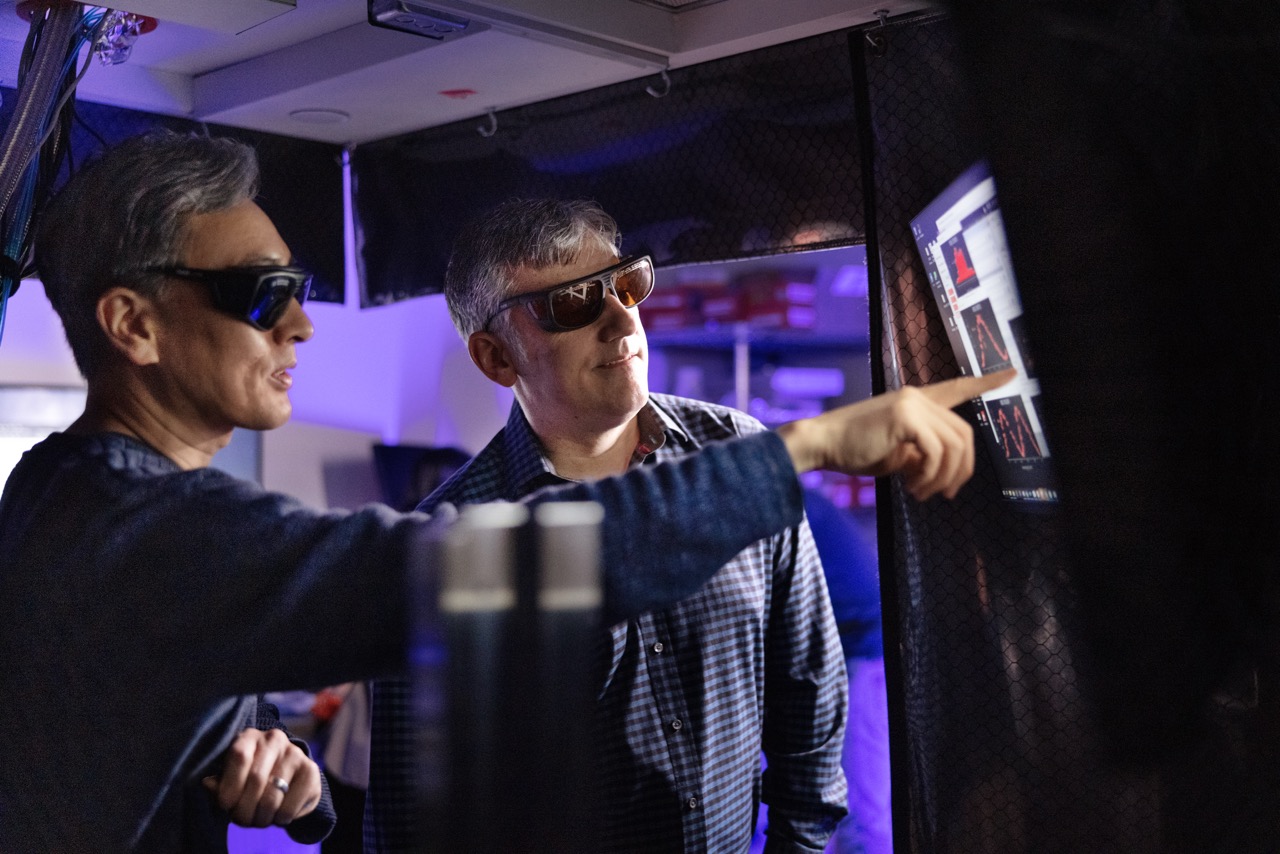Two researchers with glasses on looking at a bright screen in a dark lab
